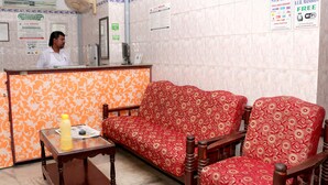 Un área de recepción con un sofá, sillas, mostrador de recepción y un ventilador.