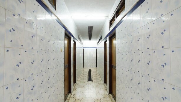 Un pasillo con paredes y suelo de baldosas, que presenta un desagüe central y puertas a ambos lados.