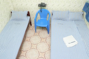 Two single beds with striped bedding, a blue plastic chair, a telephone on a stand, and a folded white towel on one bed. - SIU Mansion Lodge (Chennai)