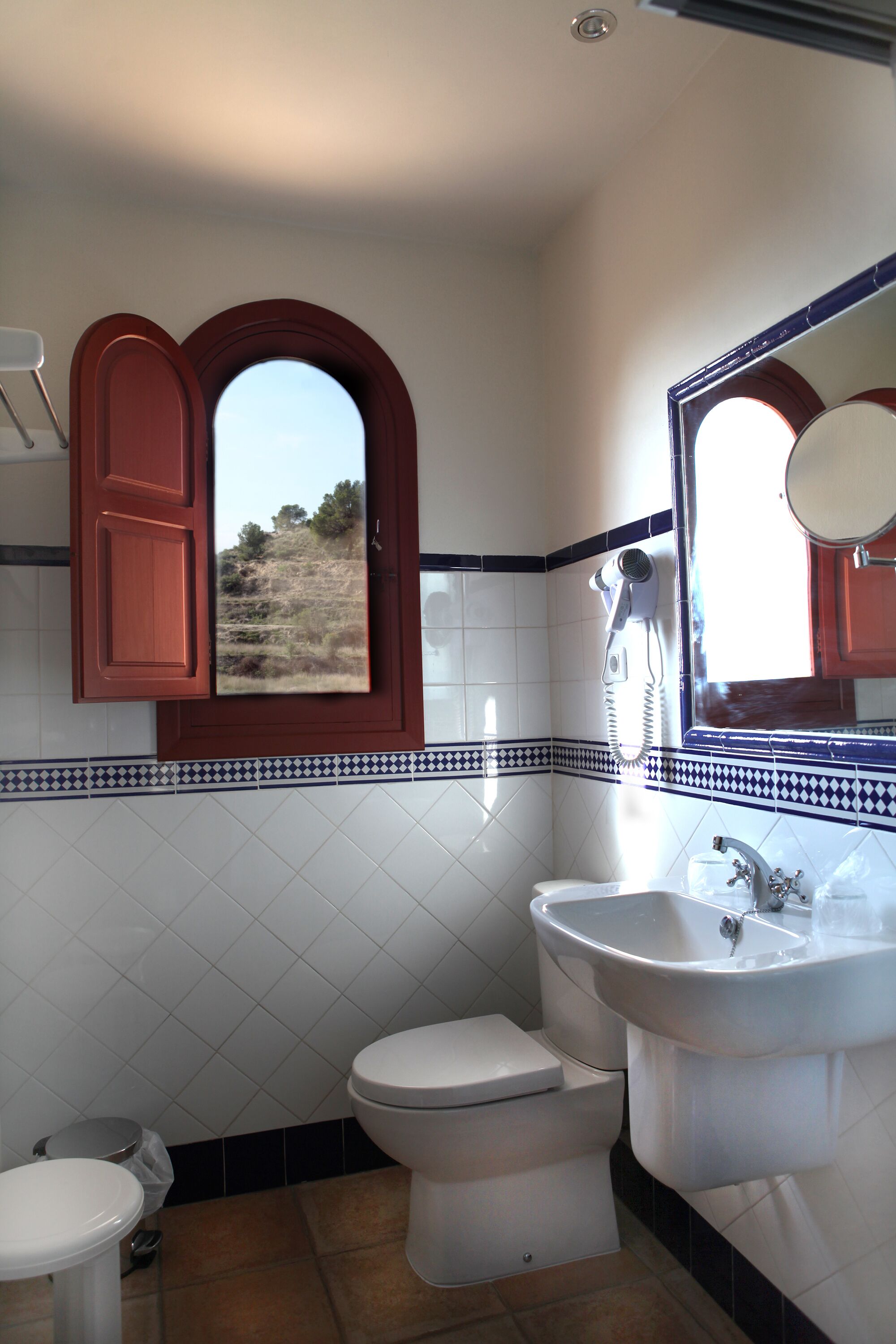 Een badkamer met toilet, wastafel en een raam met uitzicht op een landschap.