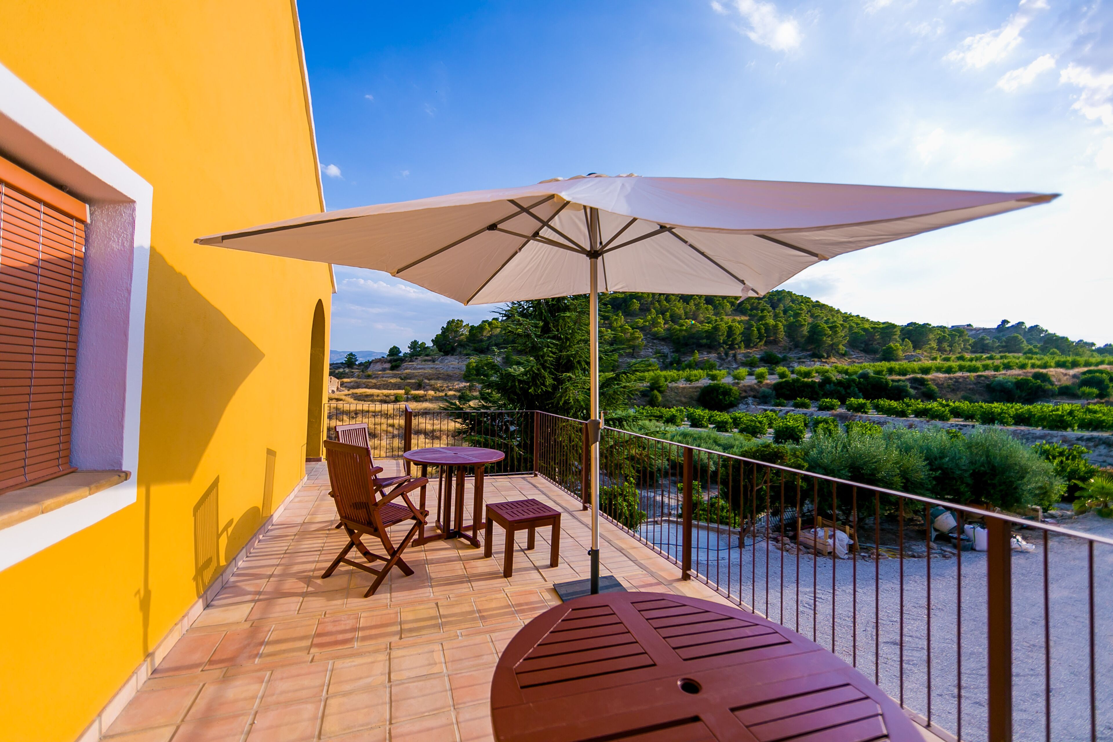 Een balkon met een tafel, stoelen, een grote parasol en uitzicht op een rivier en heuvels.