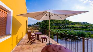 Een balkon met een tafel, stoelen, een grote parasol en uitzicht op een rivier en heuvels.