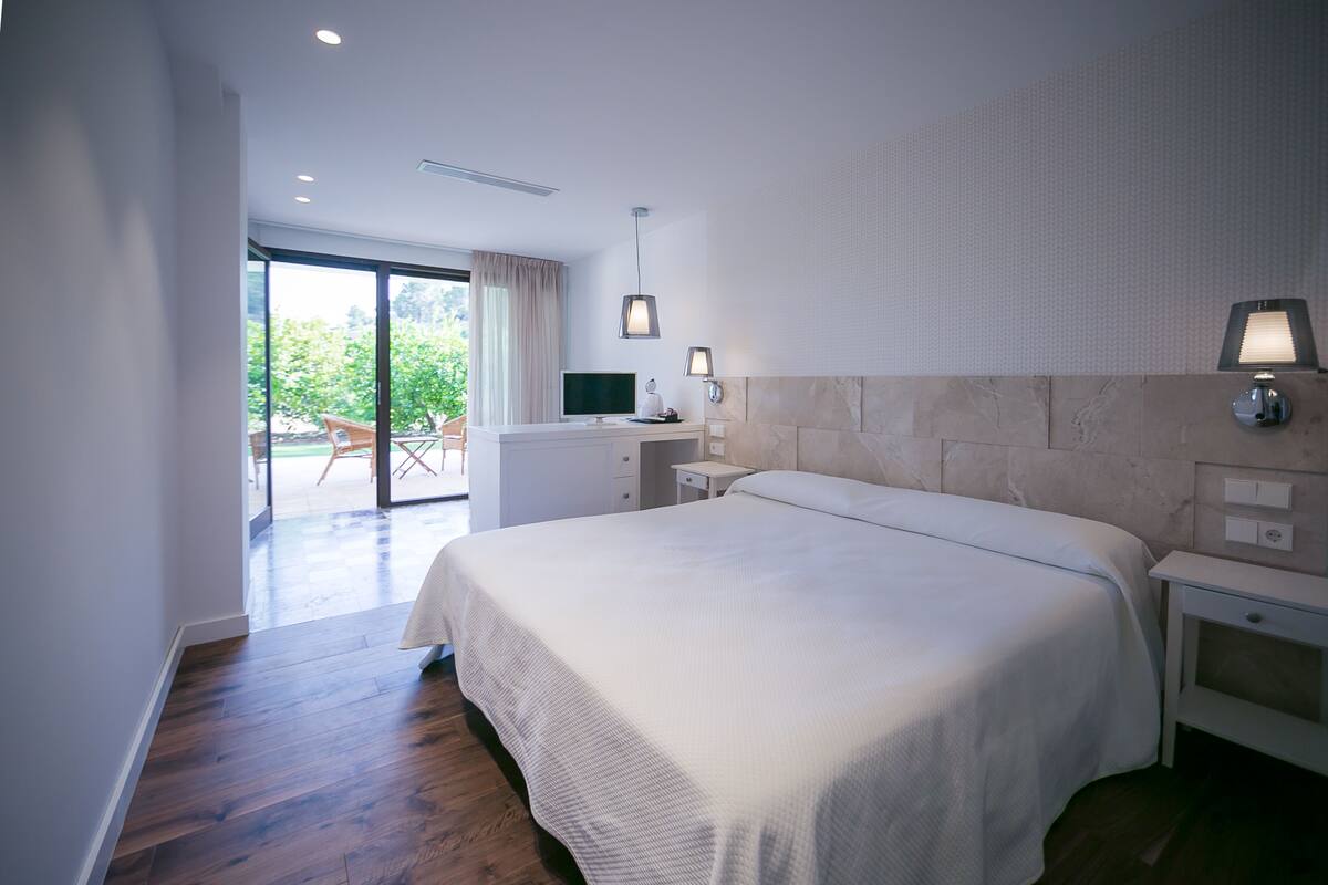 Una habitación de hotel moderna con una cama grande, un escritorio con computadora y vistas al exterior.