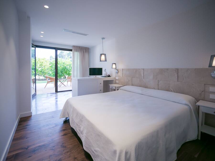 Una habitación de hotel moderna con una cama grande, un escritorio con computadora y vistas al exterior.