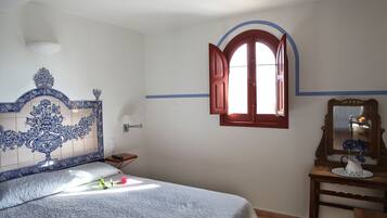 A bedroom with a bed, a nightstand, a dresser, a mirror, and a window with open shutters.