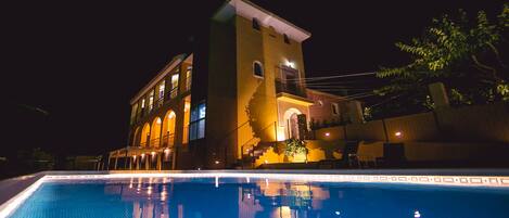 A nighttime view of a hotel with a swimming pool in the foreground.