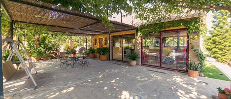 A covered patio area with stone flooring, outdoor furniture, and potted plants.