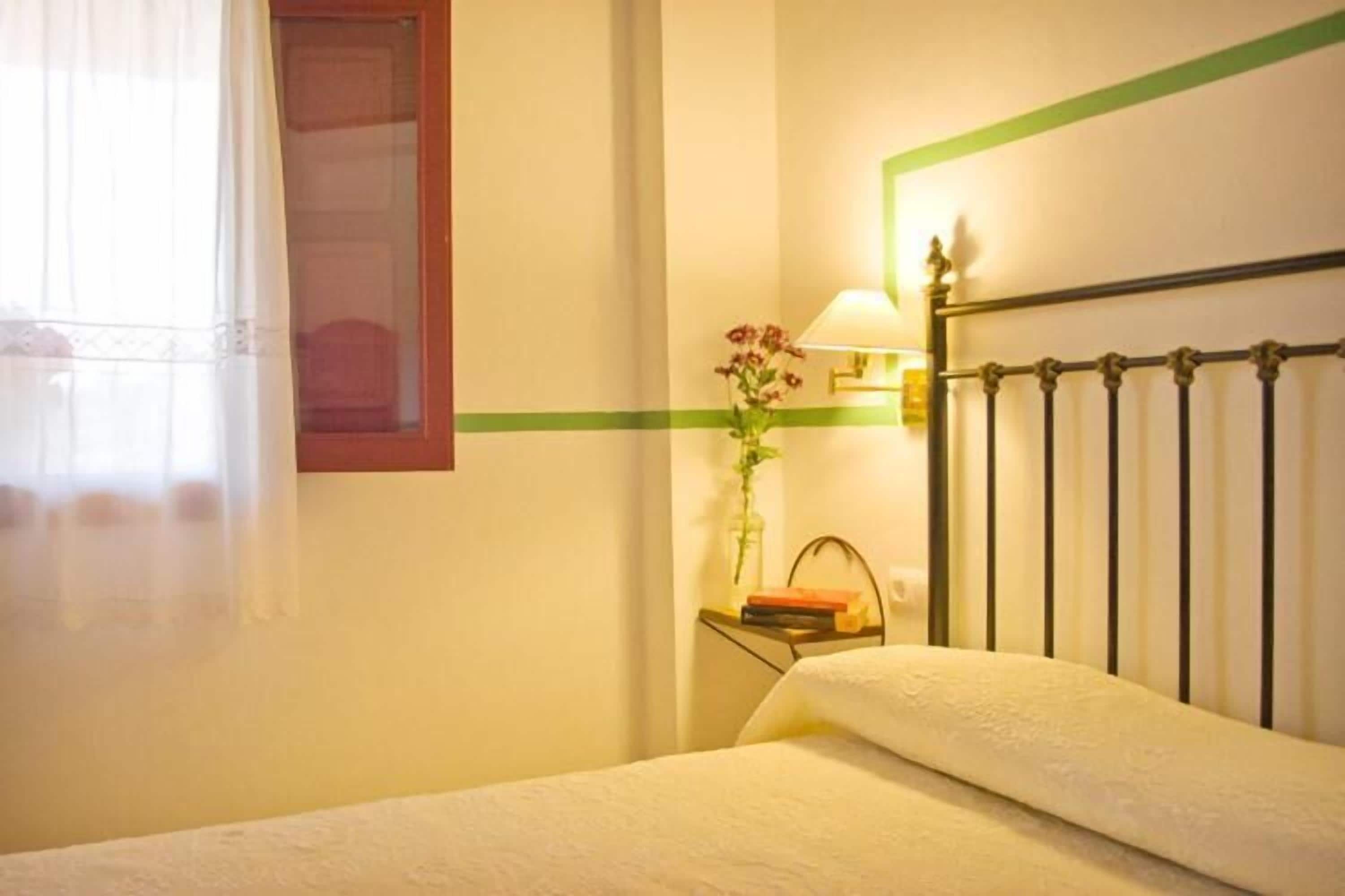 Una habitación de hotel con una cama, una mesita de noche, una lámpara y un ventanal con cortinas.