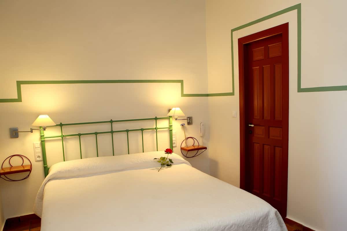 Una cama bien hecha con una colcha blanca, dos lámparas de noche y una rosa roja sobre la cama.