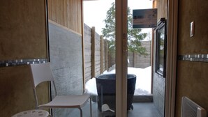 A room with a white chair, a pair of shoes, a black trash bin, and a window with a view of a wooden fence and trees. - Auberge Ninguruforet (Biei)