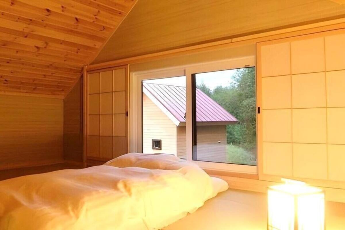 A bedroom with a bed, a window, and a view of a house.