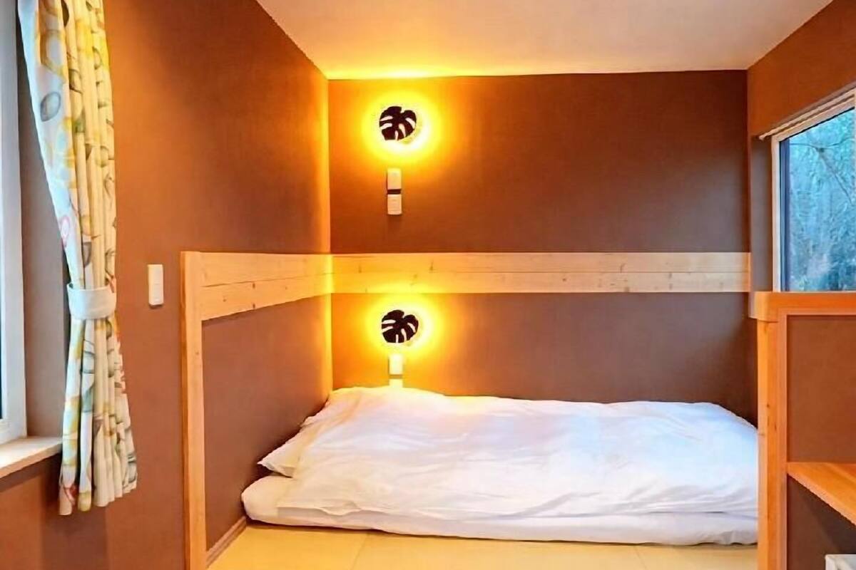 A small, single-bed room with wooden headboard and nightstands, a window with curtains, and a ceiling light.