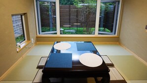 A tatami mat room with a table, a small window, and a view of a garden. - Auberge Ninguruforet (Biei)