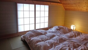 A room with tatami flooring, a bed with white bedding, a shoji screen window, and a bedside lamp. - Auberge Ninguruforet (Biei)