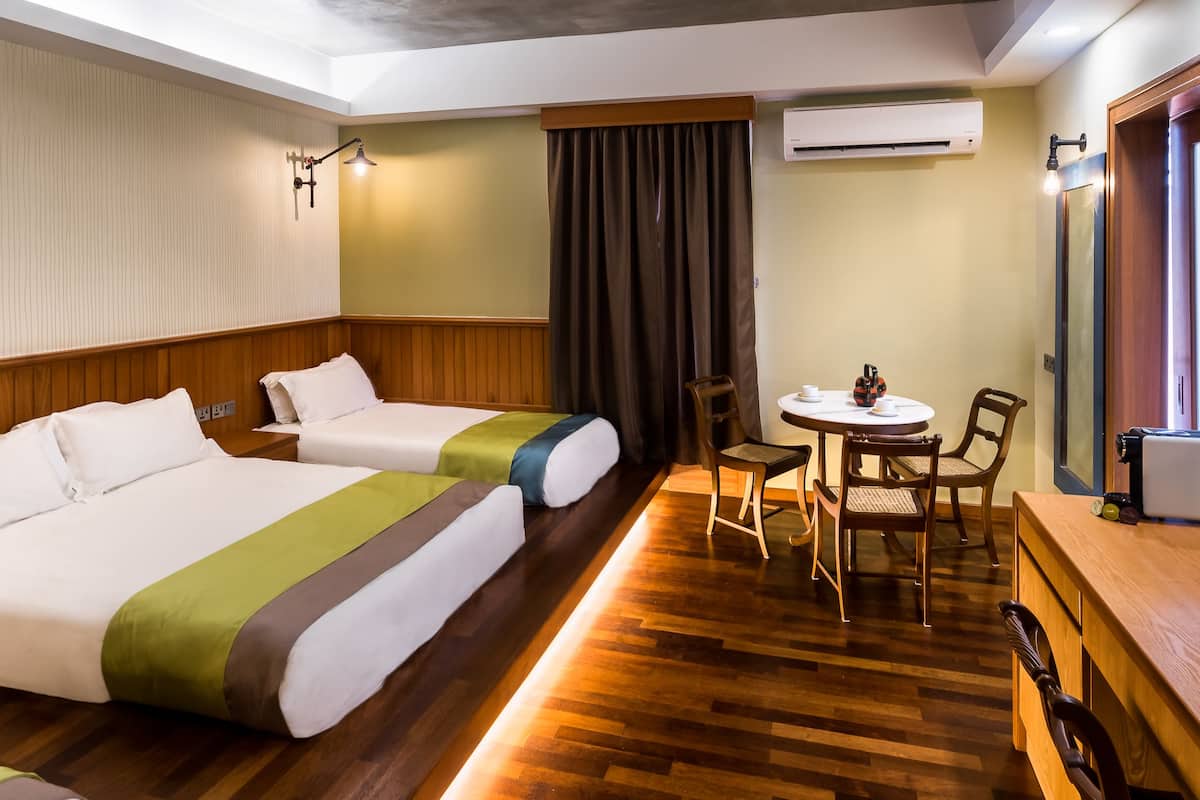 Ein Hotelzimmer mit zwei Betten, einem kleinen Tisch mit Stühlen, einer Klimaanlage und Holzböden.