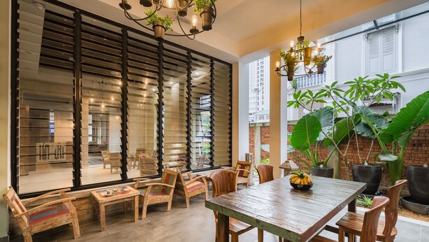 Un comedor amplio con mesa y sillas de madera, ventanas grandes con persianas y una lámpara colgante.