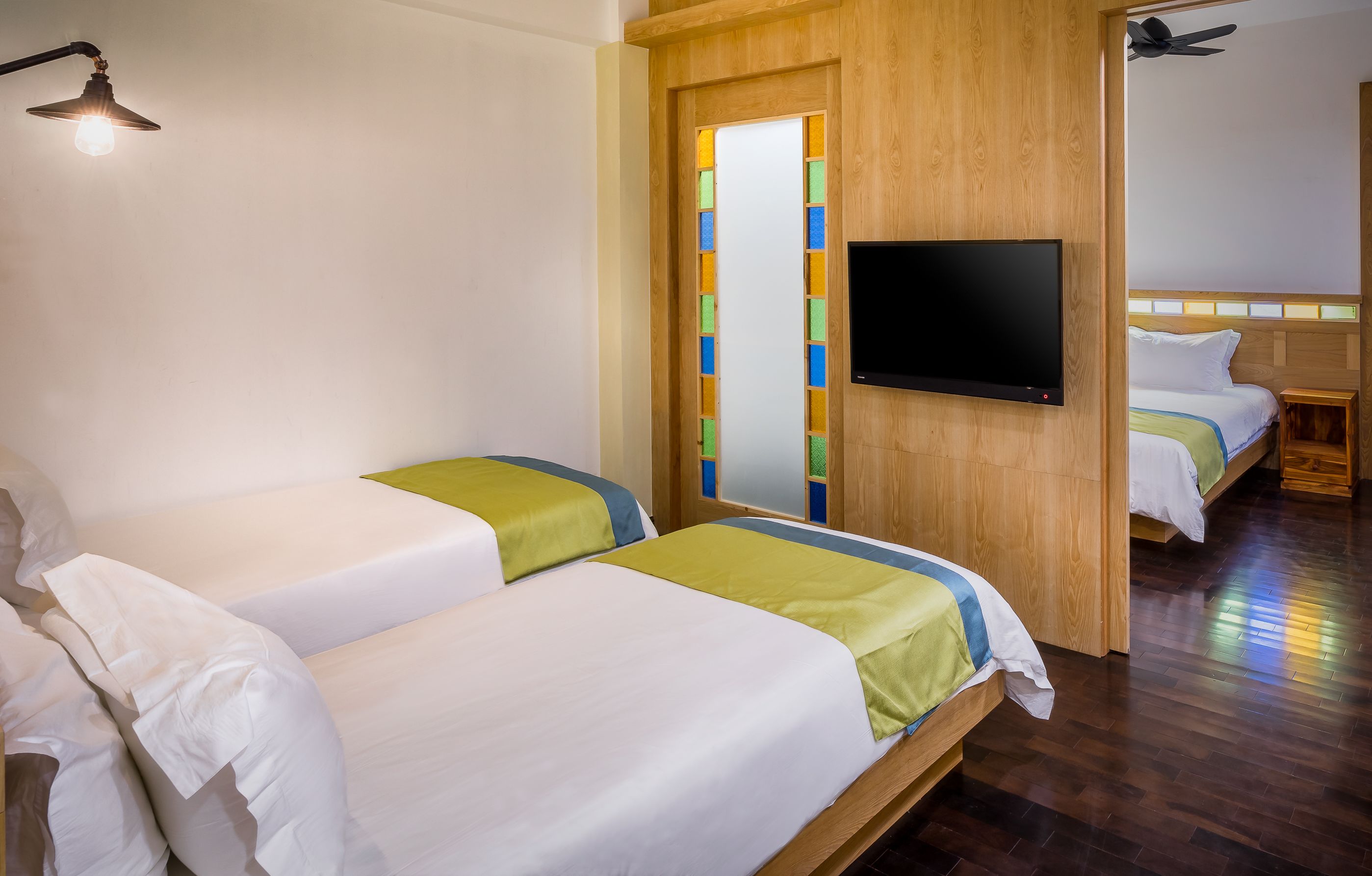 Habitación de hotel con dos camas, un televisor montado en la pared y una puerta de madera con paneles de colores.
