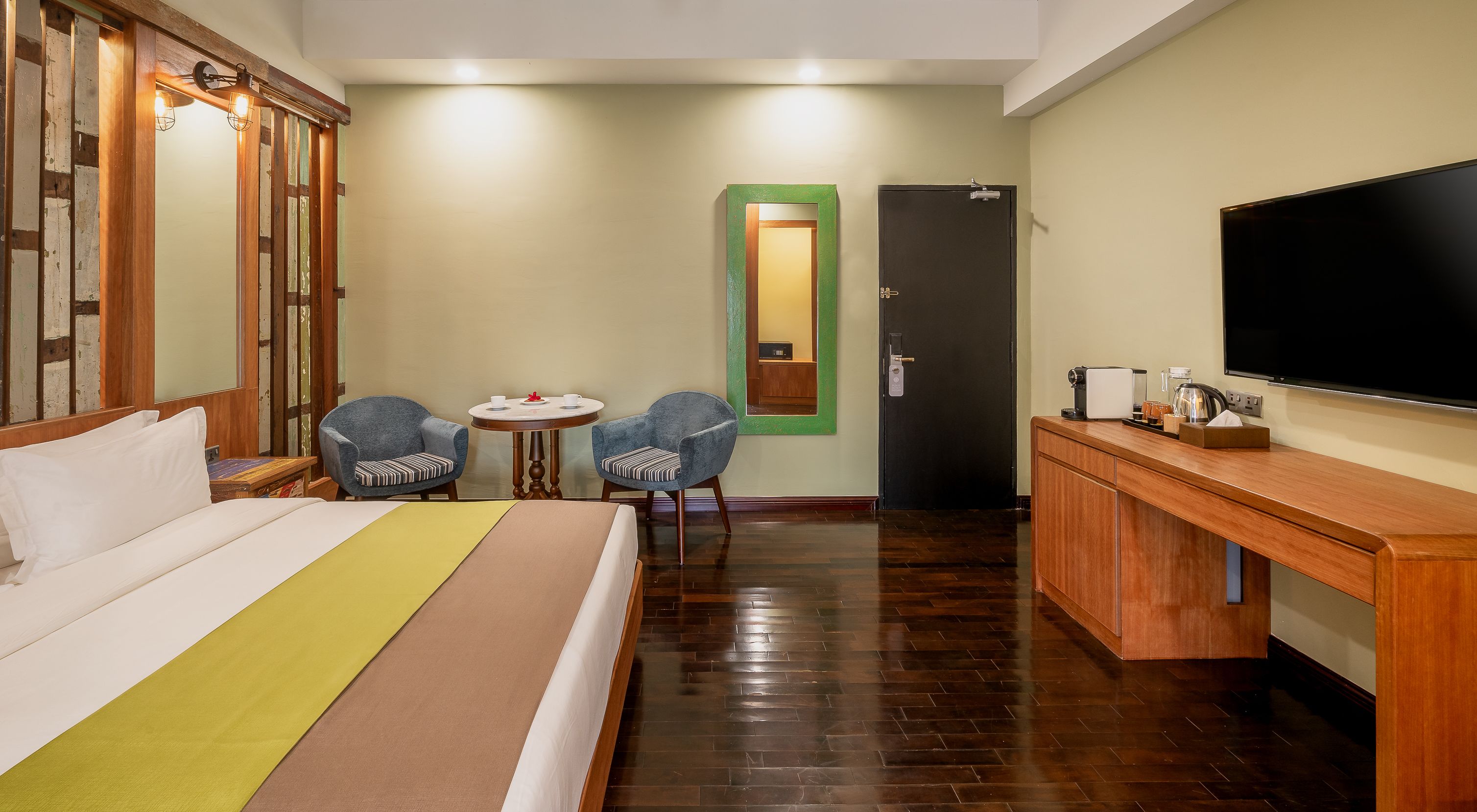 Une chambre d’hôtel comprenant un lit, deux fauteuils, une petite table, un téléviseur et un bureau en bois.