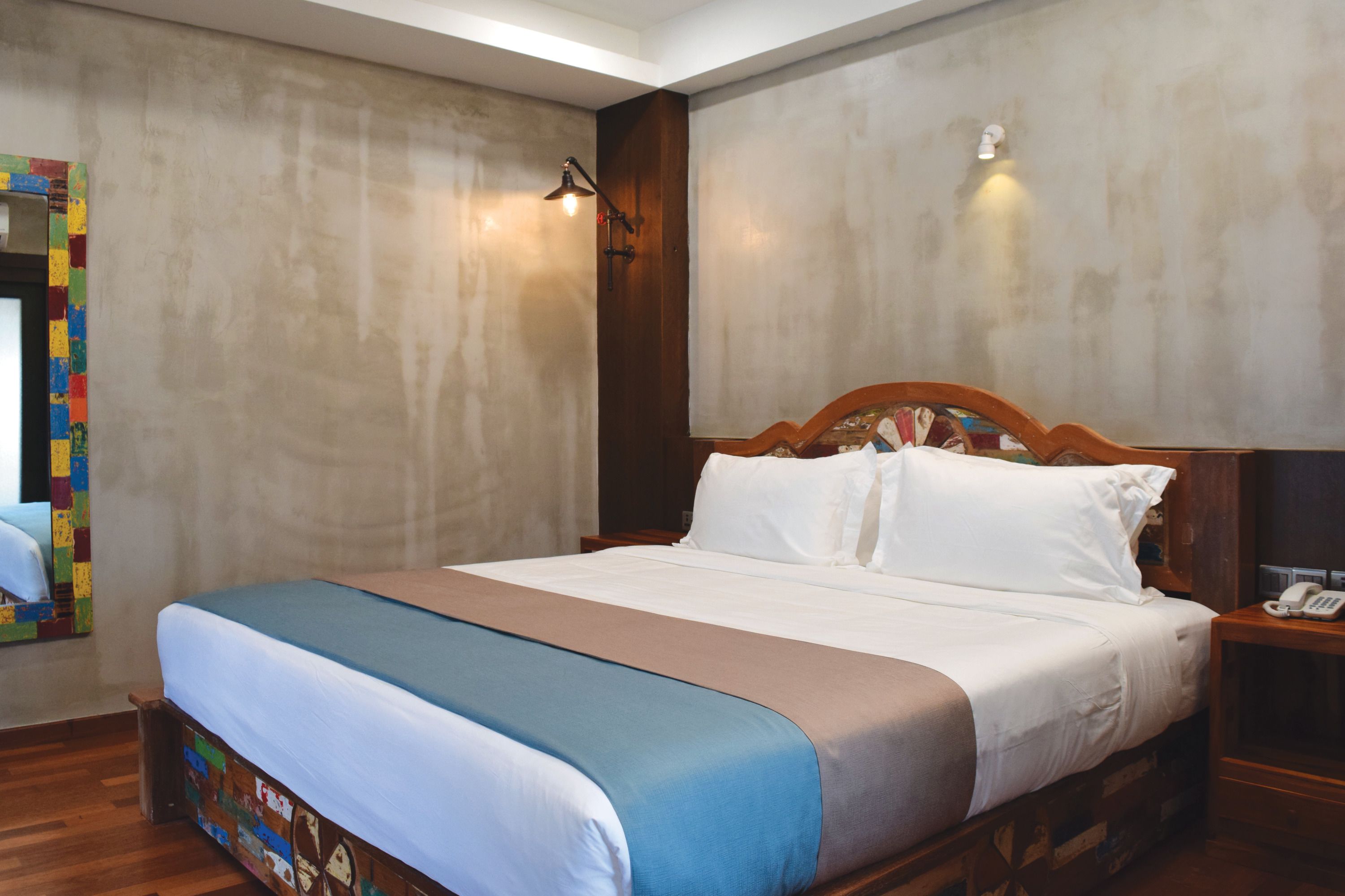 A neatly made bed with a blue and beige bedspread, a wooden headboard, and a bedside table with a telephone.