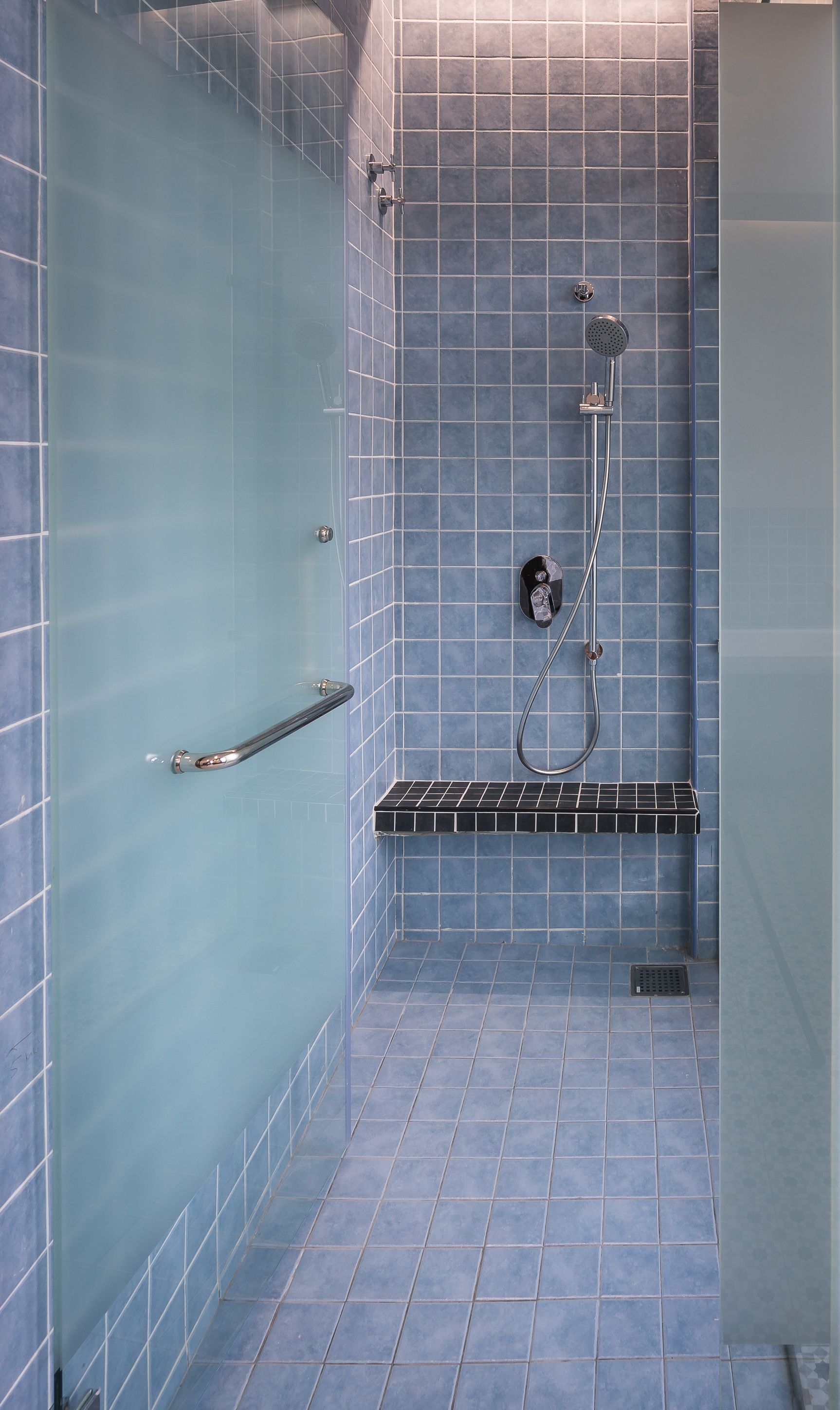 A modern bathroom with a glass shower enclosure, a handheld showerhead, and a built-in seat.