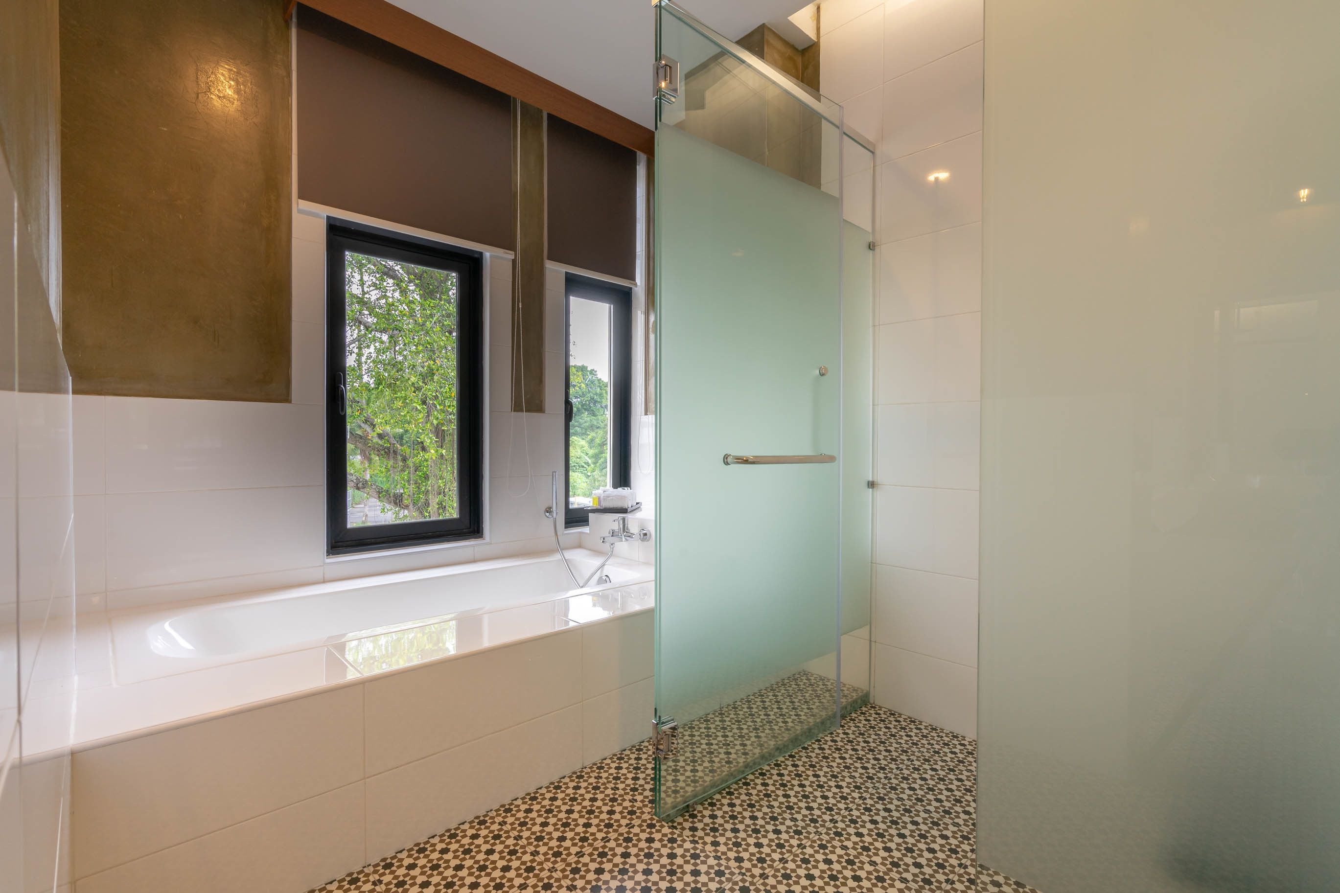 A modern bathroom with a glass shower enclosure, a bathtub, and a window providing a view of greenery.