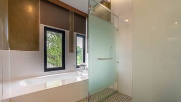 A modern bathroom with a glass shower enclosure, a bathtub, and a window providing a view of greenery.