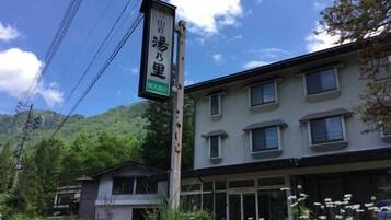 A building with a signboard, surrounded by greenery and a mountain in the background.