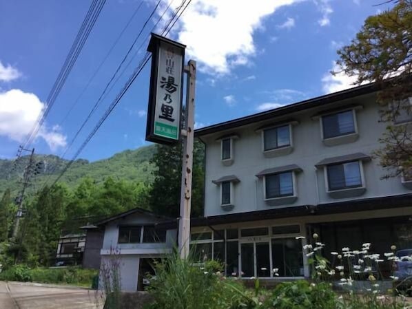 A building with a signboard, surrounded by greenery and a mountain in the background. - Sanso Yunosato (Takayama)