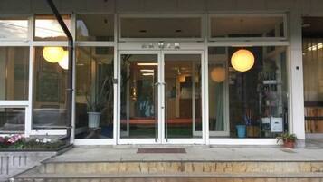 A building with a glass entrance, steps leading up to it, and potted plants on the ground.