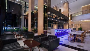 A modern hotel lobby with leather sofas, wooden tables, and a bar area. - Harper Cikarang by ASTON (Cikarang)