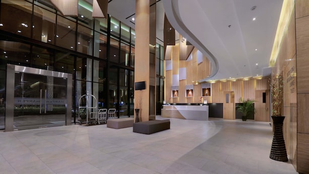 A spacious lobby with a reception desk, seating area, and a large glass wall. - Harper Cikarang by ASTON (Cikarang)