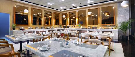 A hotel dining area with multiple tables set for guests, equipped with cutlery, plates, and napkins.