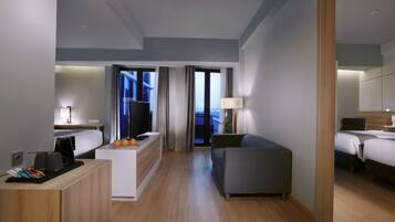 Quarto de hotel moderno com cama, sofá, escrivaninha com cafeteira e televisão.
