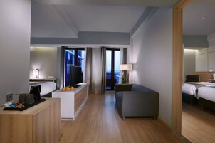 Quarto de hotel moderno com cama, sofá, escrivaninha com cafeteira e televisão.