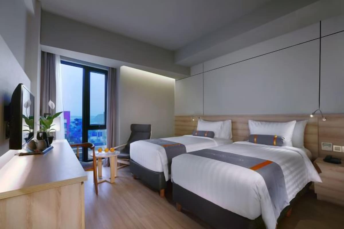 A modern hotel room with two beds, a desk, and a chair.