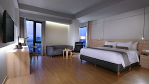 A modern hotel room with a large bed, a sofa, a small table, and a TV. - Harper Cikarang by ASTON (Cikarang)