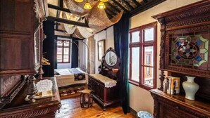 Une pièce avec un plancher en bois, un lit, une commode, un miroir et une fenêtre à vitraux.