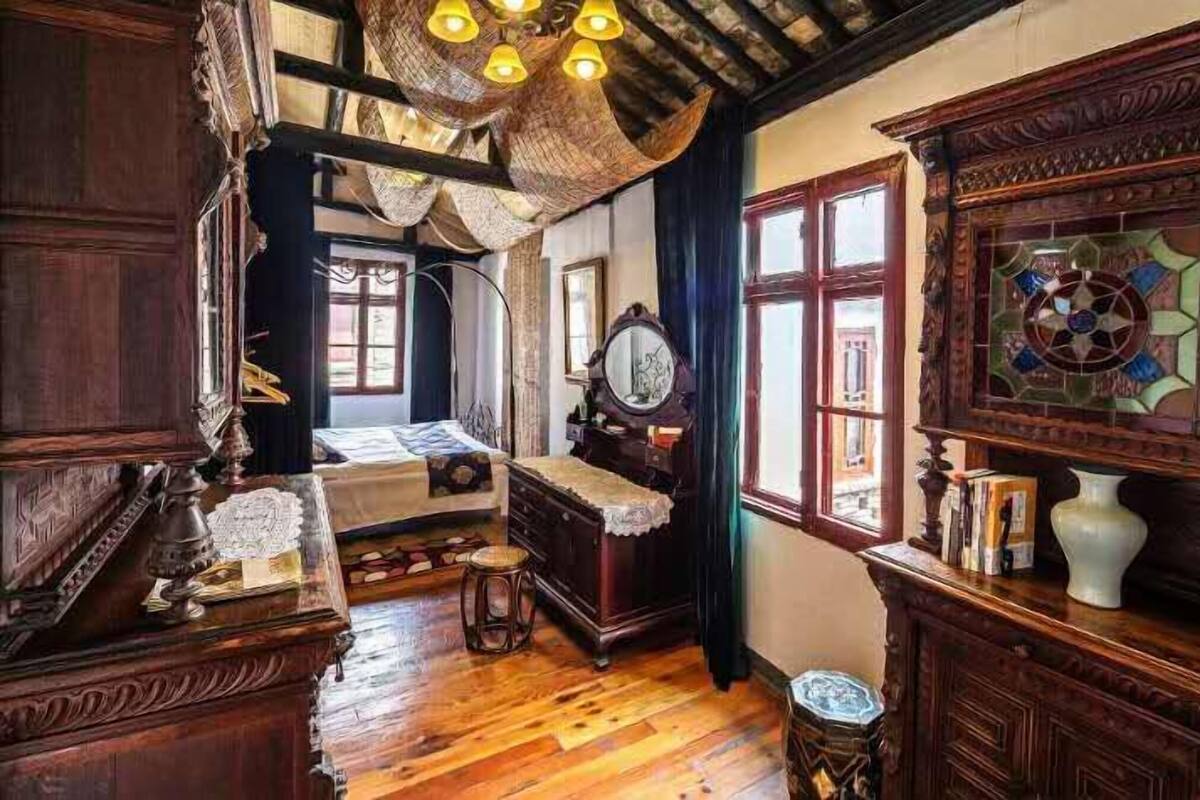 Ein Zimmer mit Holzboden, einem Bett, einem Schminktisch und einem Spiegel, sowie einem Buntglasfenster.
