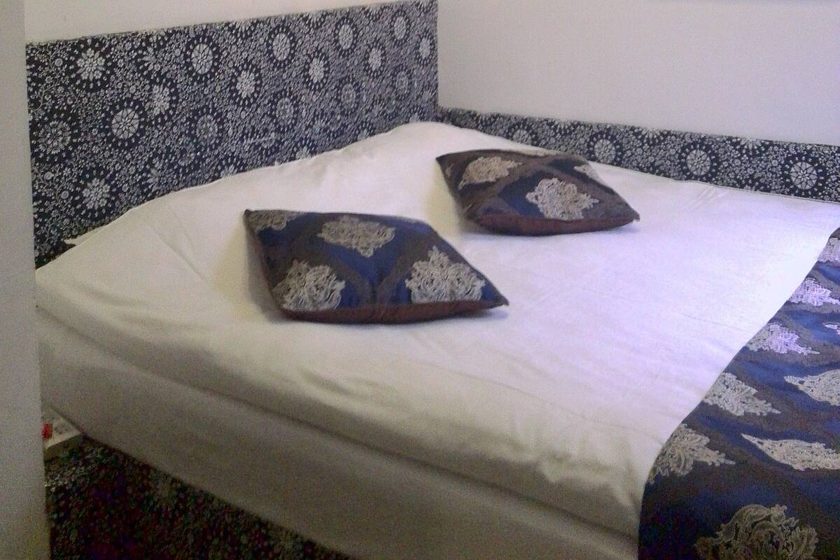 Ein Bett mit einem gemusterten Kopfteil, einer Wanddekoration und einem gerahmten Poster.