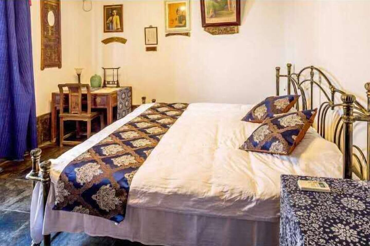 Ein Schlafzimmer mit einem Bett, einem Holzstuhl, einem kleinen Tisch und einer Wand mit gerahmten Bildern.