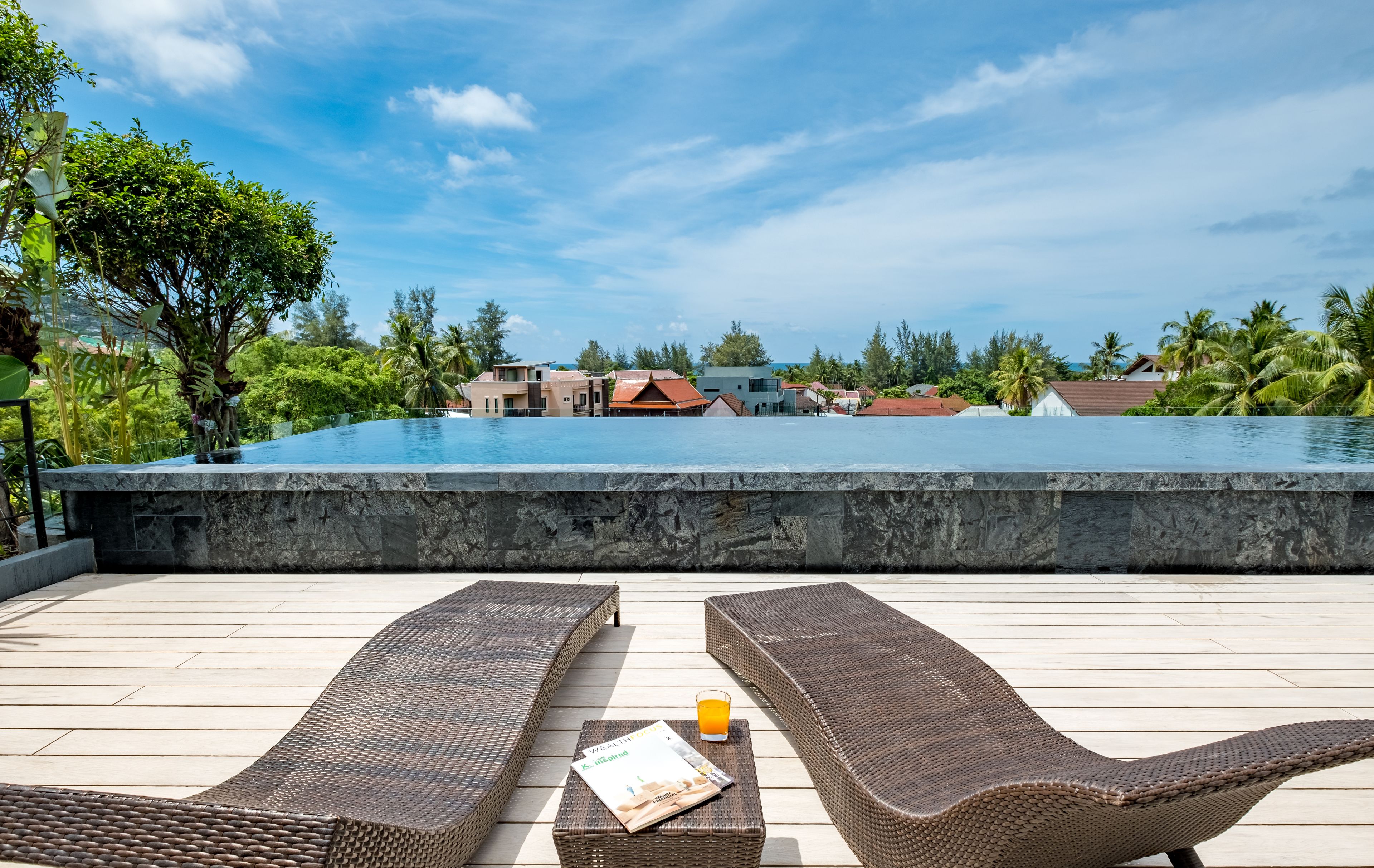 Un espace aménagé au bord de la piscine, avec des chaises longues et un bar, offrant une vue sur la piscine et un quartier résidentiel.