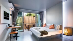 A modern hotel room with a large bed, a desk with a chair, a small table, and a balcony with a wooden fence. - Kamala Resotel (Kamala)