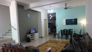 A living room with a sofa, a TV, a dining area with chairs, a kitchen in the background, and a staircase. - Salam Homestay d'Sendayan (Bandar Sri Sendayan)