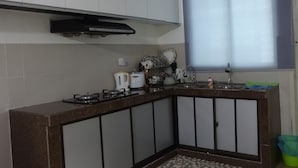 A compact kitchen with white cabinets, a dark countertop, and a window with blinds. - Salam Homestay d'Sendayan (Bandar Sri Sendayan)