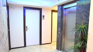 A hallway with two doors, one with a visible elevator button, and a potted plant. - Kayislioglu Hotel (Burdur)