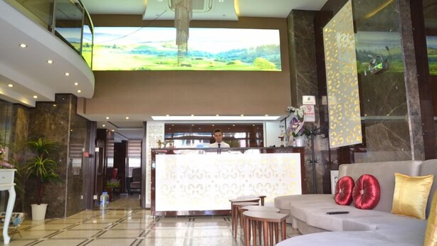 A hotel lobby with a reception desk, seating area, and a large screen displaying a landscape. - Kayislioglu Hotel (Burdur)