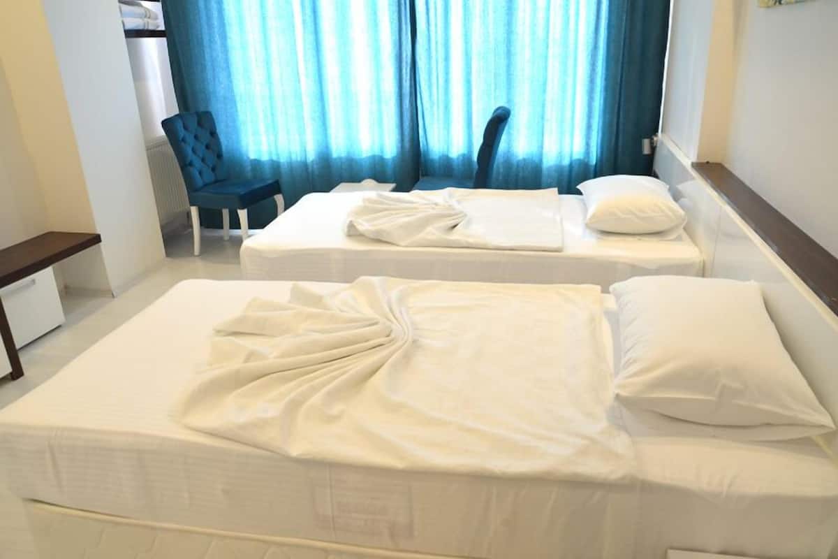 A hotel room with two beds, a chair, and a window with blue curtains.