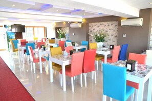 Une salle à manger bien éclairée, avec des tables et des chaises blanches, et des chaises de différentes couleurs.