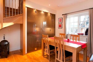 Un comedor con una mesa y sillas de madera, una mesa decorada con camino de mesa rojo y una ventana con cortinas.