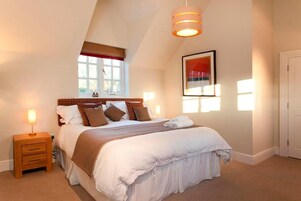 A neatly arranged bedroom with a large bed, a bedside table, a hanging light fixture, and a window with curtains.